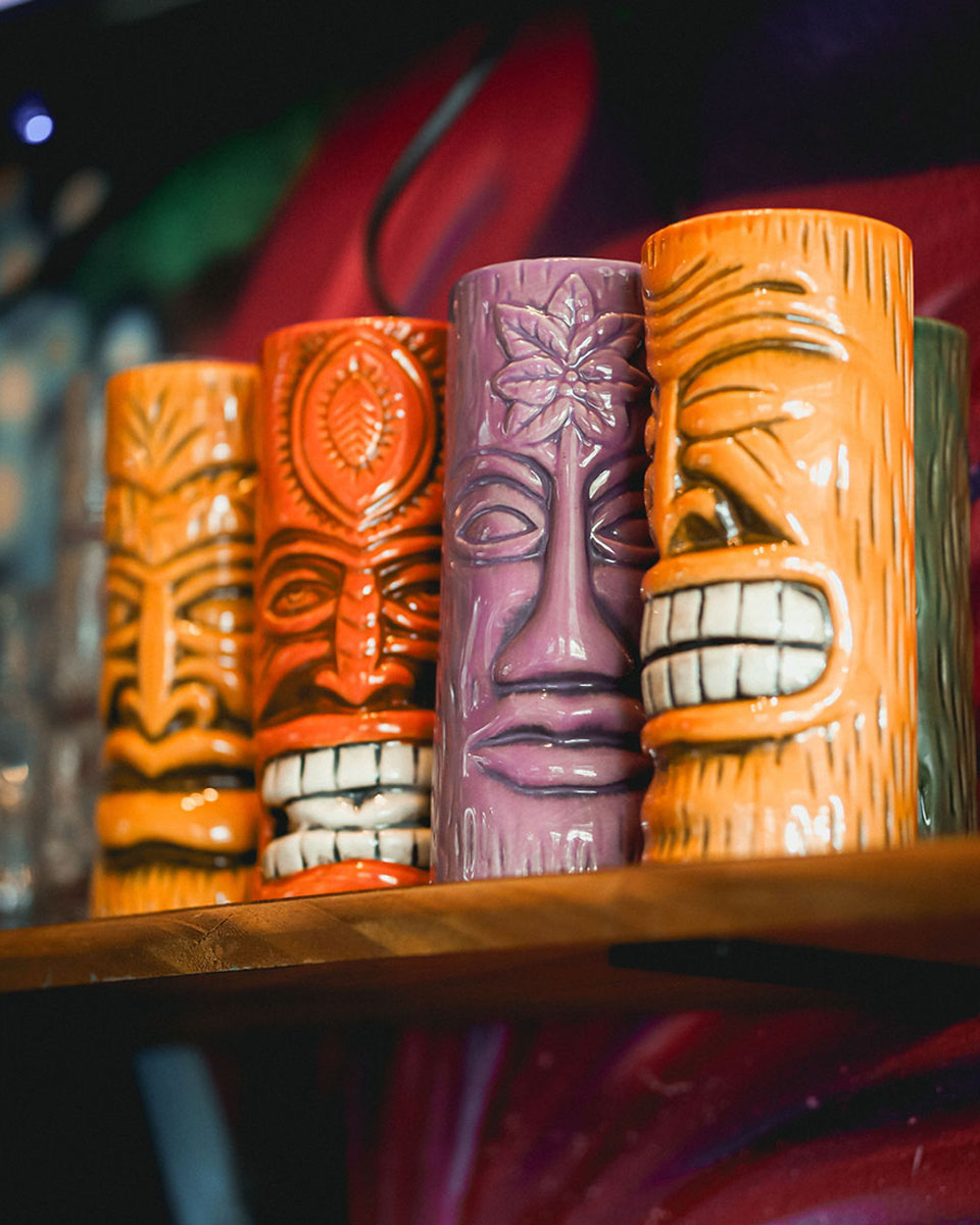 A set of 4 Tiki Cocktail glasses on a shelf.