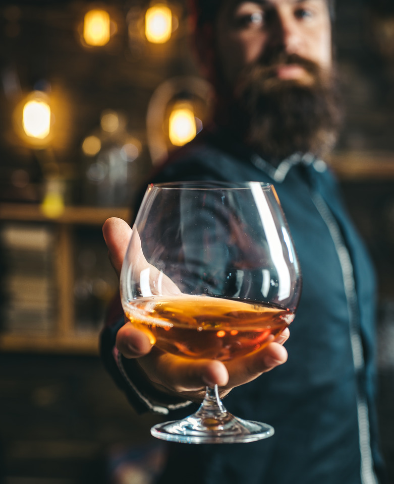 A focused shot of an alcoholic drink, with a man holding it in the background.